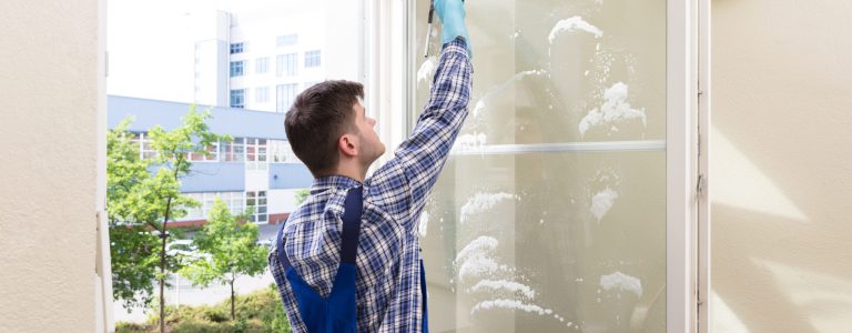 Rear,View,Of,A,Young,Male,Housekeeper,Cleaning,Window